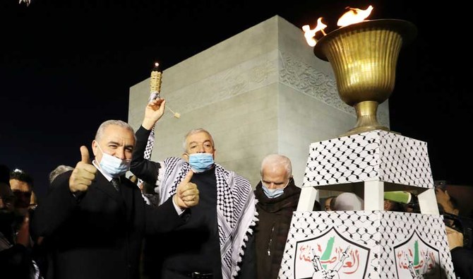 Palestinian Prime Minister Mohammad Shtayyeh (L) and Deputy Chairman of the Fatah movement, Mahmoud Al-Aloul (C) gesture after lighting a torch at the presidential headquarters in the West Bank town of Ramallah, to mark the 56th anniversary of the launching of the Fatah movement. (AFP)