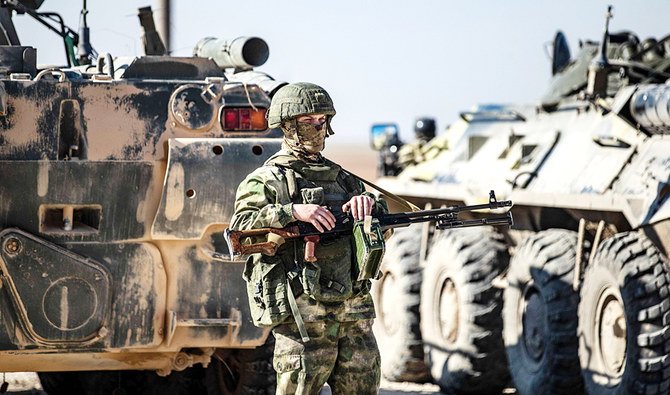 A Russian soldier stands guard as troops accompany a convoy of displaced Syrian civilians leaving for their homes in the northern town of Ain Issa in the countryside of the Raqqa region. (AFP)