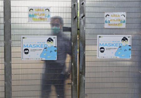 A warden looks from behind the gate of Gunung Sindur Prison covered with coronavirus awareness posters. Indonesia's highest Islamic body on Friday gave its religious approval to China's Sinovac vaccine, paving the way for its distribution in the world's most populous Muslim nation. (AP)
