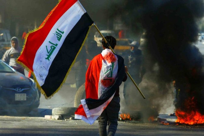 A demonstrator carries an Iraqi flag as he walks near burning tires, during an anti-government protest in Najaf, Iraq, January 12, 2020. (Reuters)