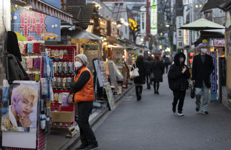 A sales person, wearing a face mask, stands outside as people walk on a street in a neighborhood dubbed 