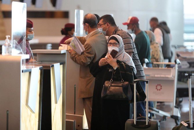 Travellers, mask-clad due to the COVID-19 coronavirus pandemic, wait at the Qatar Airways check-in desk ahead of a flight at Hamad International Airport near the Qatari capital Doha on January 18, 2021. (AFP)