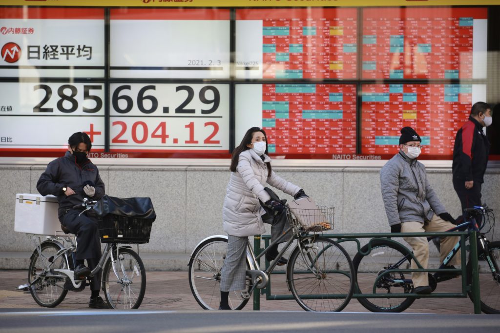 People riding their bicycles wait for the signal to change to green in front of an electronic stock board of a securities firm in Tokyo, Wednesday, Feb. 3, 2021. Asian shares opened mostly higher on Wednesday although markets in Shanghai and Hong Kong were lower. (AP Photo/Koji Sasahara)