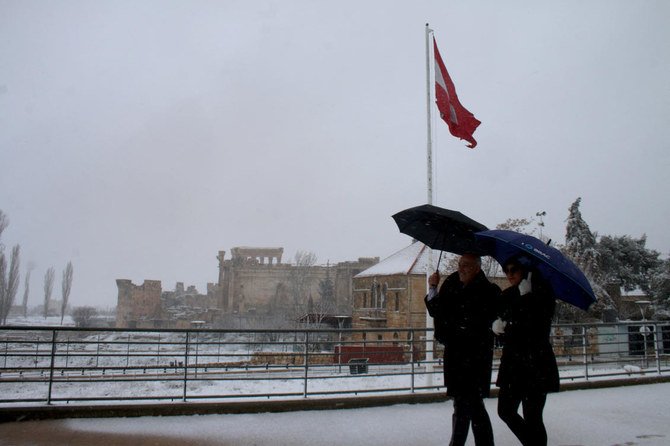 A couple walks along the historic site of Baalbek during snowfall in Lebanon's eastern Bekaa Valley, on February 17, 2021. (AFP)