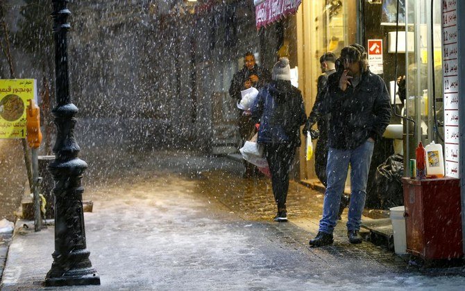 People walk in the street during snowfall in the West Bank city of Ramallah on February 17, 2021. (AFP)