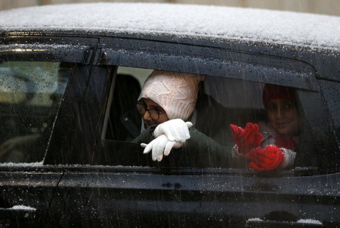 Children try to catch snow flakes from a car window during snowfall in the West Bank city of Ramallah on February 17, 2021. (AFP)
