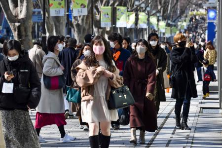 People wearing face masks walk along a street in the Harajuku shopping district in Tokyo on February 27, 2021. (AFP)