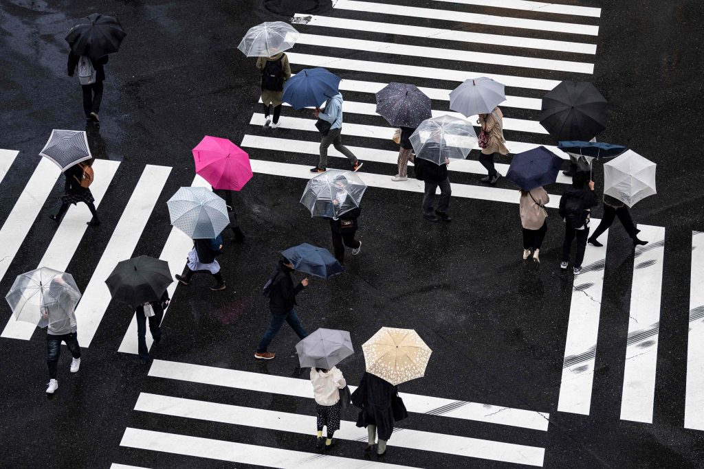 People cross a street during a rainy afternoon in Tokyo, on March 21, 2021. (File photo/AFP)