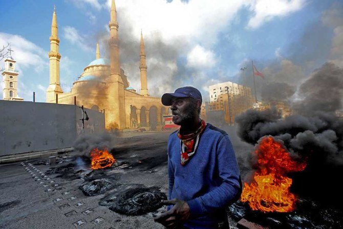 A man stands next to flaming tires at a make-shift roadblock set-up by anti-government demonstrators next to the Mohammed al-Amin Mosque in the Martyrs' Square in the centre of Lebanon's capital Beirut on March 8, 2021. (AFP)