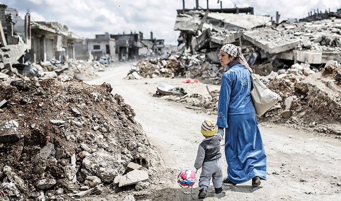 A Kurdish woman walks with her child past the ruins of the town of Kobani. (AFP)