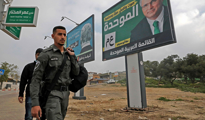 An Israeli border policeman walks past campaign posters for the Joint List and the United Arab List in the Bedouin town of Rahat near the southern Israeli city of Beersheba on March 7, 2021, ahead of the legislative election. (AFP)