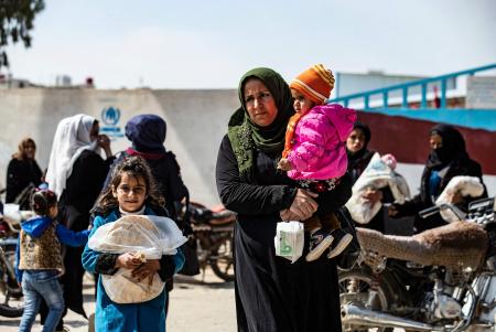 A Syrian woman walks with her children while in a commercial district in Syria's northeastern city of Qamishli on March 9, 2021. (AFP)