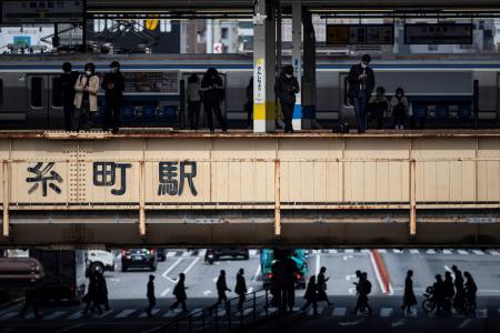 People wait for a train on a platform (top) while people cross a street below in Tokyo on March 5, 2021. (AFP)
