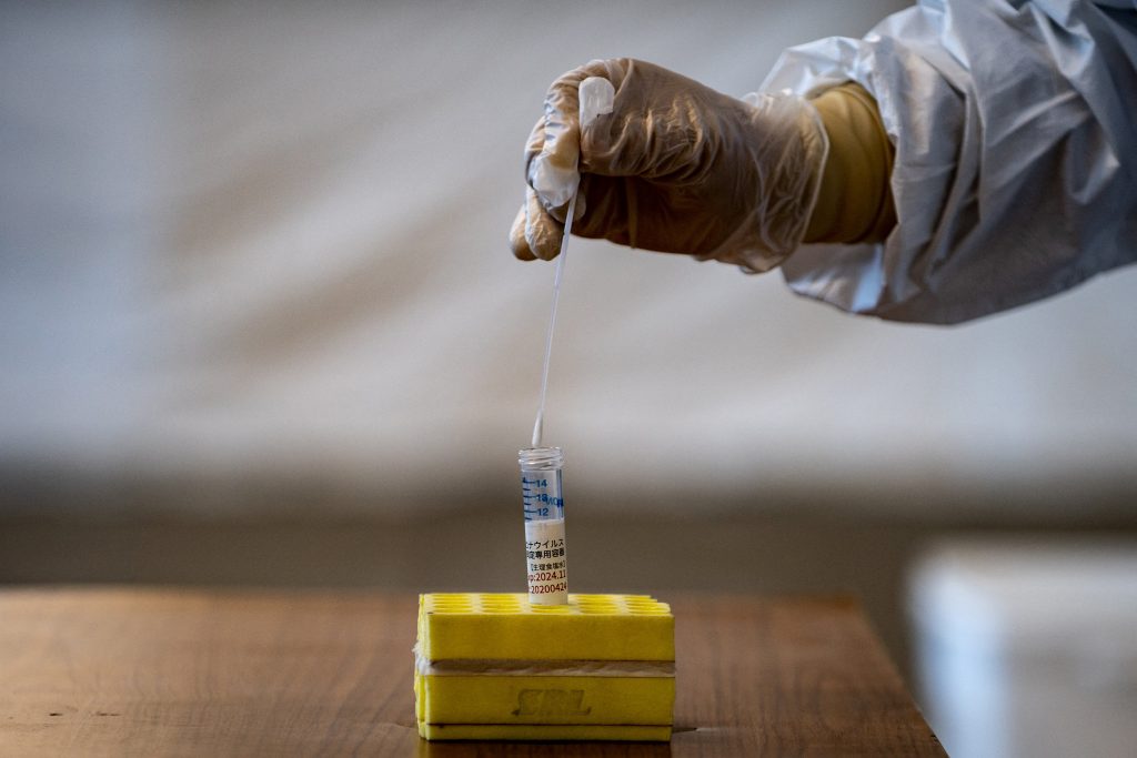 A medical staff wearing protective clothing puts a swab into a container during demonstration of the polymerase chain reaction (PCR) swab test for the COVID-19 coronavirus in Tokyo. (AFP)