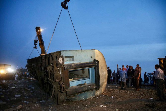 People stand by as a telescopic railway crane lifts an overturned passenger carriage in Toukh in Egypt’s central Nile Delta province of Qalyubiya on April 18, 2021. (AFP)