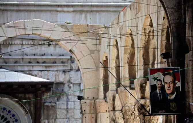 A poster depicting Syria's President Bashar al-Assad and his father and predecessor Hafez al-Assad hangs along an alley in Damascus on April 21, 2021. (AFP/LOUAI BESHARA)