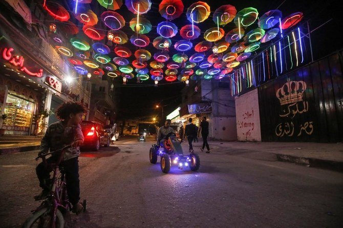 Young Palestinians ride a bicycle and a mini pedal-powered car along a street decorated with lit up umbrellas in Rafah. (File/AFP)