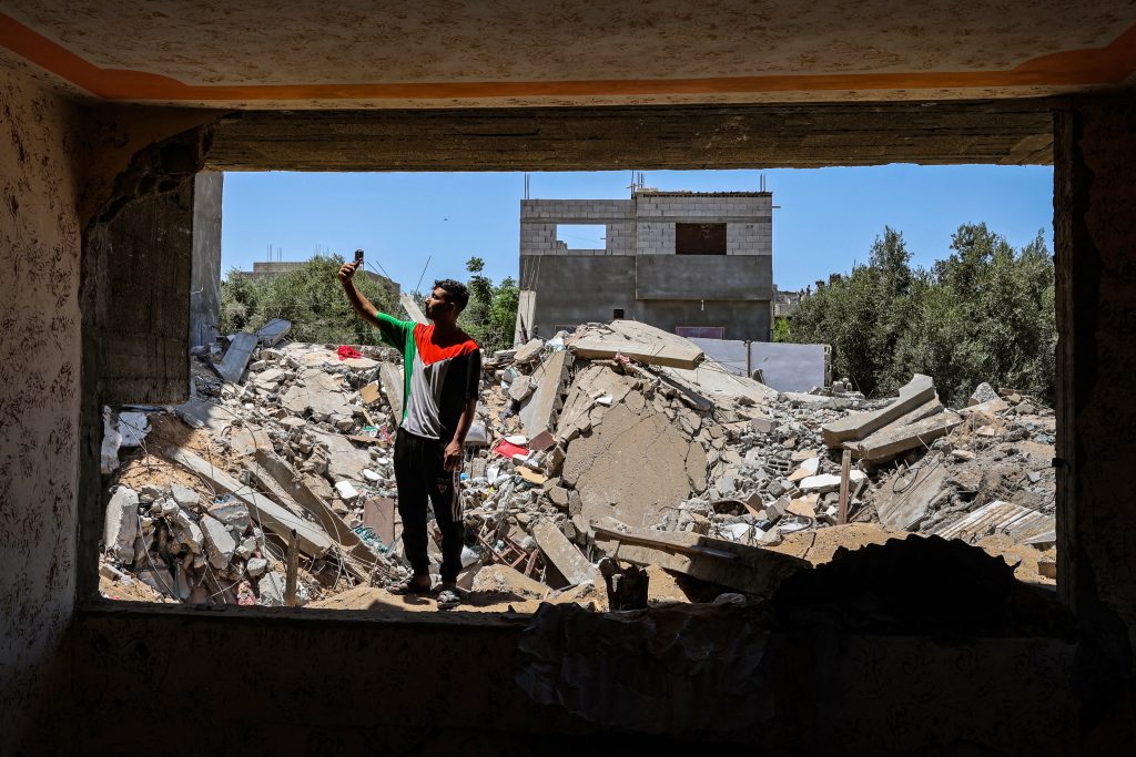 A Palestinian youth takes a selfie picture in front of his destroyed house in Khan Yunis in the southern Gaza Strip, which was targeted by Israeli air strikes, on May 26, 2021. (AFP)
