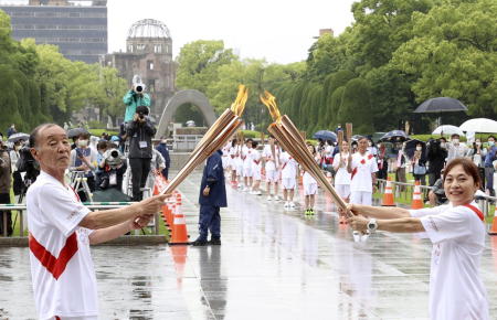 Torchbearers hand over the flame of the Olympic torch in the Hiroshima Peace Memorial Park as the Hiroshima Atomic Bomb Dome is seen in the background on Monday. (AFP)