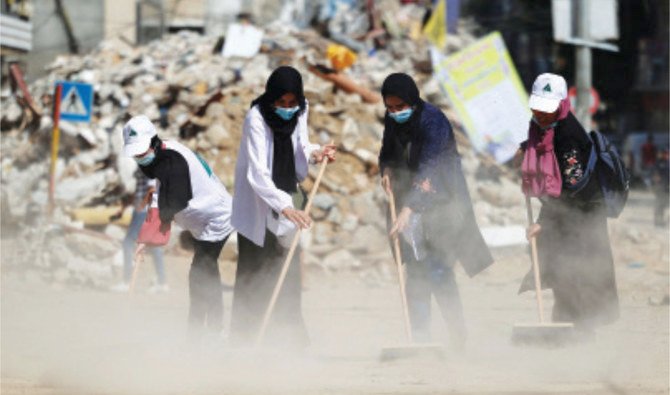 Palestinian volunteers in Gaza City’s Rimal district, on Tuesday, sweep the rubble of buildings and shops, recently destroyed by Israeli airstrikes. (AFP)