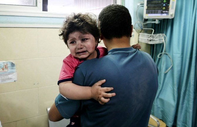 A Palestinian man holds an injured girl awaiting medical care at al-Shifa hospital, after an Israeli air strike in Gaza city, on May 11, 2021. (File/AFP)