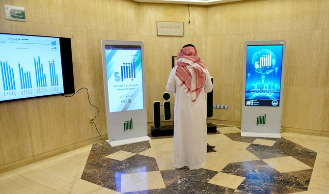 A Saudi Interior Ministry employee stands in front of a screen displaying the Absher mobile app logo at the ministry in Riyadh on February 19, 2019. (AFP)