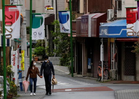 A couple wearing protective face masks, amid the coronavirus disease (COVID-19) pandemic, make their way at a local shopping street decorated with Tokyo 2020 Olympic Games flags in Tokyo, Japan, May 5, 2021. (Reuters)