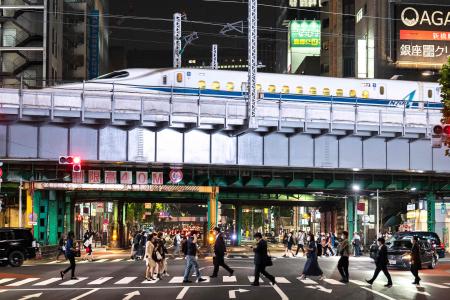 People cross a street as a shinkansen, or high speed bullet train, arrives in Tokyo on May 19, 2021. (AFP)