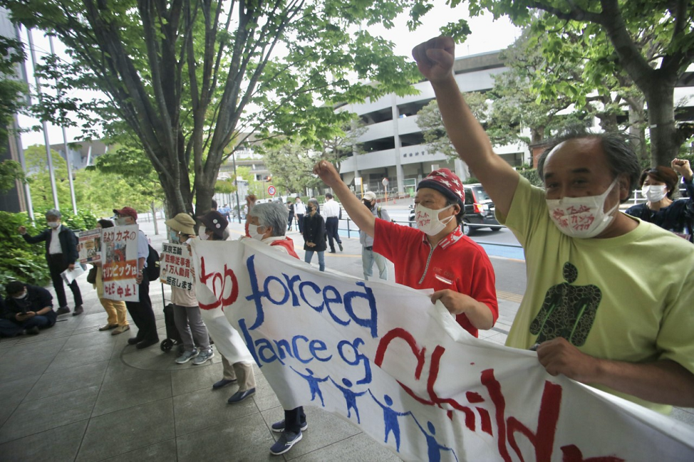 On May 18, protesters opposed to the Olympic Games, held a banner in front of the Japan Olympic Committee headquarters in Tokyo. One banner demands the end to the “forced attendance” of children at Games events. (ANJ photo)
