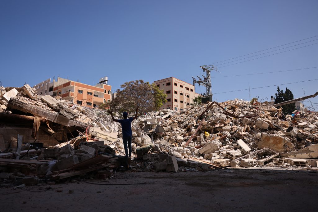 A Palestinian man gestures as he stands next to a building a day after its destruction in Israeli air raids in Gaza City, May. 18, 2021. (AFP)
