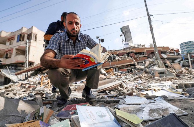 A Palestinian man browses through a book he found amid the rubble of the Kuhail building, which housed Samir Mansour’s bookstore in Gaza City. (AFP)
