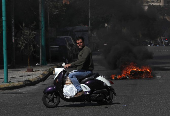 A man riding scooter carries bread while passing near burning tires to block a main road in Beirut in March. Tuesday, Lebanon’s economy ministry raised the price of subsidized bread for the fifth time in a year. (AP)