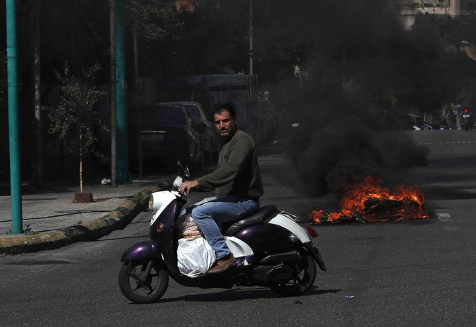 A man riding scooter carries bread while passing near burning tires to block a main road in Beirut in March. Tuesday, Lebanon’s economy ministry raised the price of subsidized bread for the fifth time in a year. (AP)