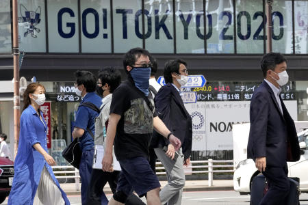 Passers-by cross a street with a backdrop of an Olympics ad sign in Tokyo. (AP)