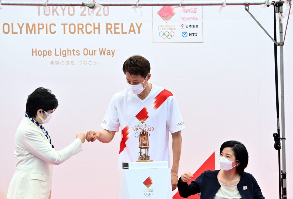 Tokyo governor Yuriko Koike (L), fist bumps with former Japanese professional tennis player and torchbearer Shuzo Matsuoka (C) next to the Olympic lantern as former Japanese Paralympian Aki Taguchi (R) looks on during the unveiling ceremony of the Olympic flame at the Komazawa Olympic Park General Sports Ground,Tokyo, July. 9, 2021. (AFP)