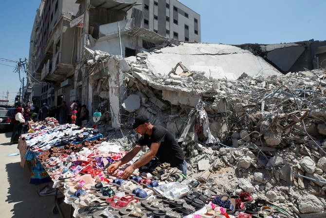A Palestinian sells shoes on a stall near the rubble of his old shoe store that has been destroyed in an Israeli air strike, ahead of the Eid Al-Adha holiday, in Gaza City, July 14, 2021. (Reuters)