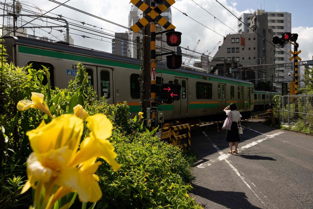 A pedestrian waits at a train level crossing in the Yoyogi neighborhood of Tokyo on July 17, 2021. / AFP / Yuki IWAMURA