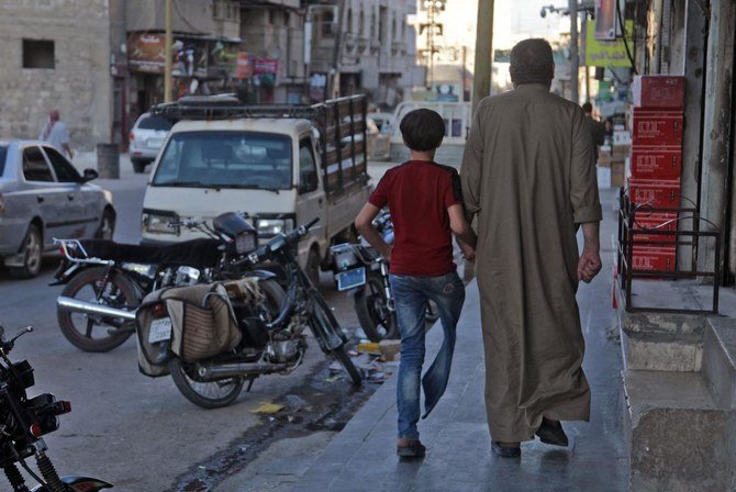 Displaced Syrian Mustafa Shaaban Abu Khalil walks alongside his son who lost a leg due to bombing, on a street in the rebel-held city of al-Bab northwest of Aleppo in northern Syria, on June 23, 2021. (AFP)
