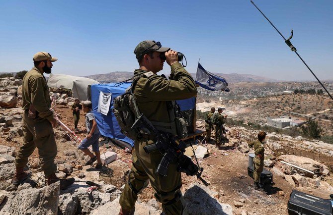 Israeli soldiers observe the Palestinian village of Beita with binoculars as settlers evacuate the newly-established wildcat outpost of Eviatar in Beita, near Nablus in the occupied West Bank. (File/AFP)