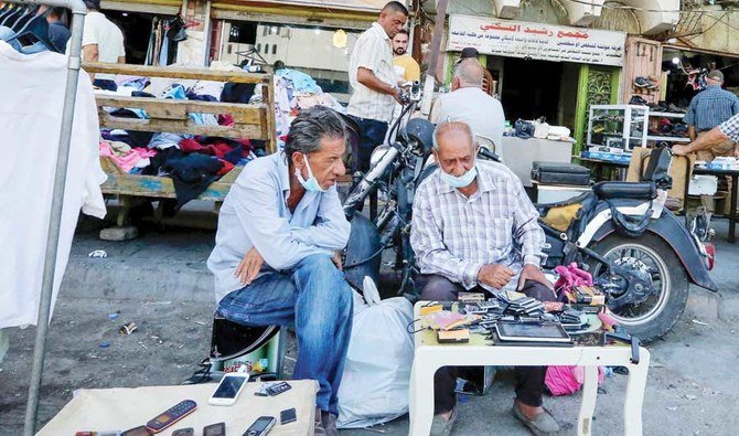 An Iraqi shopkeeper wearing a face mask speaks with a customer at his stall on a market street in the capital Baghdad, on July 12, 2021. (AFP)