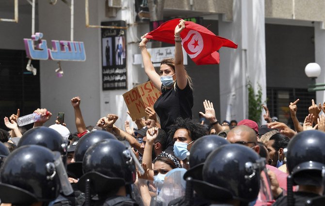 A Tunisian protester lifts a national flag at an anti-government rally as security forces block off the road in front of the Parliament in the capital Tunis on July 25, 2021. (AFP)