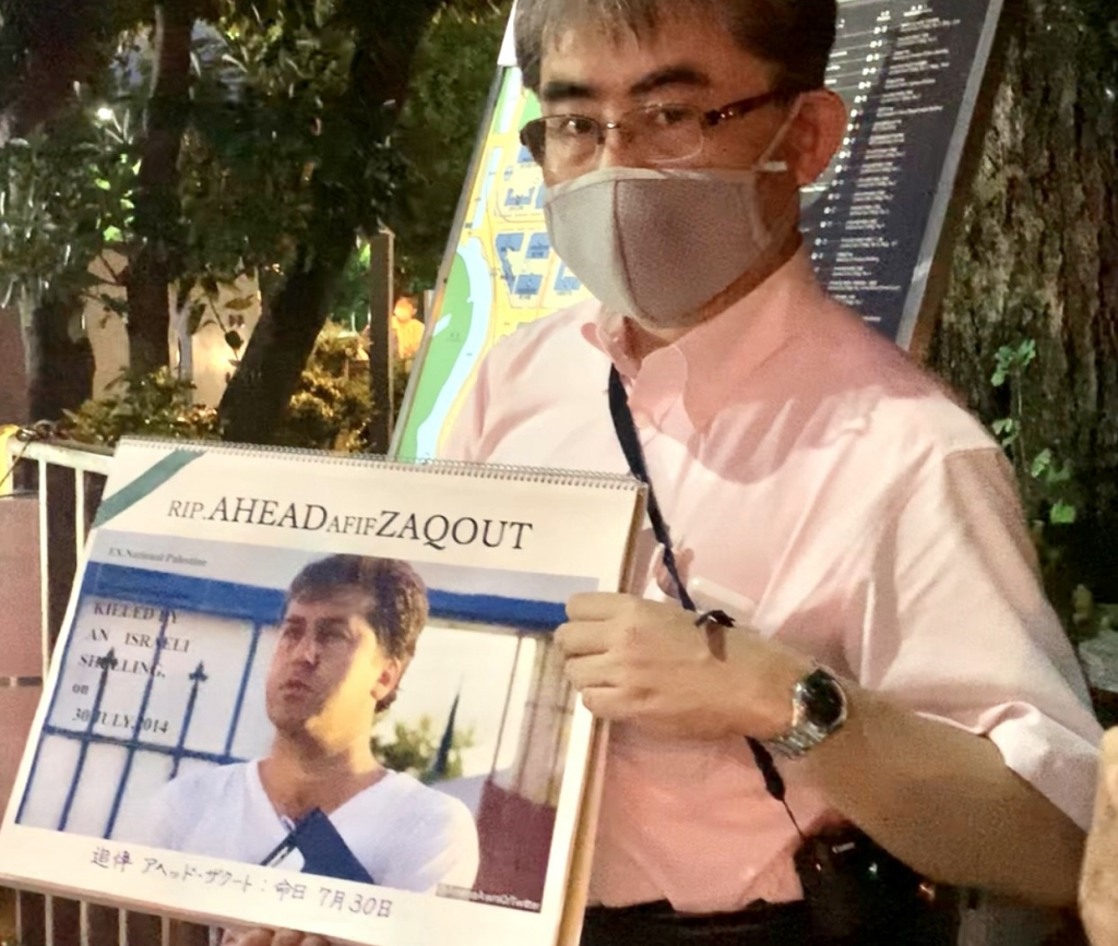 A Japanese protestor carries a poster says “Ahead Zaqout. Palestinian footballer killed by Israel” (ANJ/ Pierre Boutier)