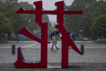 People wearing protective masks walk past a public art display of a Chinese character for flower on Sunday, July 4, 2021, in Tokyo. (AP)