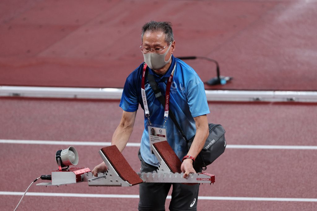 An ederly volunteer sets up a track starting block during the athletics event of the Tokyo 2020 Olympic Games at the Olympic Stadium. (AFP)