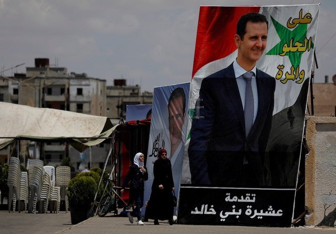 People walk past posters depciting Syria's President Bashar al-Assad, in the district of al-Waer. (Reuters)