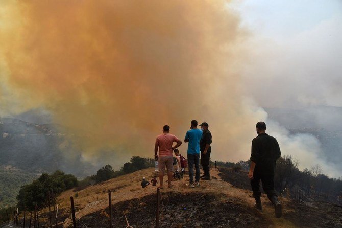 Villagers gather as smoke billows from a fire in the forested hills of the Kabylie region, east of the Algerian capital Algiers, on August 12, 2021. (AFP)