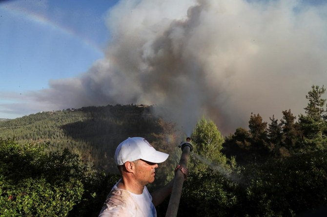 Ariel Monin sprays water over bushes at his village of Shoeva as firefighting planes and firefighters try to extinguish wildfire from getting closer to the village at the outskirts of Jerusalem August 15, 2021. (Reuters)