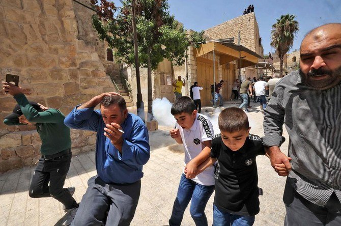 Palestinian worshipers run to avoid tear gas amid clashes with Israeli security forces at a demonstration following the Friday prayers at the Ibrahimi mosque in the occupied West Bank on August 13, 2021. (AFP)