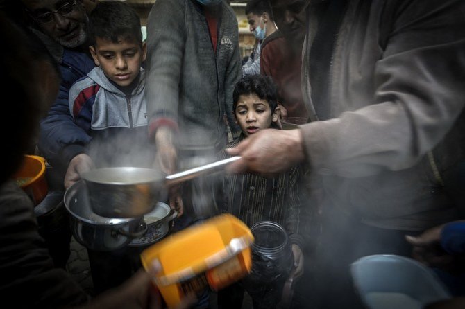 A boy waits as Palestinian Walid al-Hattab (R) distributes soup to people in need during the Muslim fasting month of Ramadan in Gaza City on April 14, 2021, amid the COVID-19 pandemic. (AFP/File Photo)