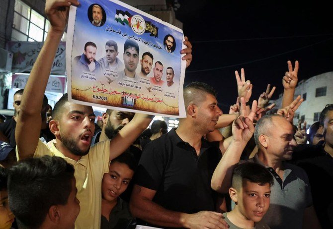 A Palestinian man flashes a poster by the militant group Islamic Jihad of 6 Palestinians who escaped from an Israeli prison, as people celebrate in the Jenin camp in the northern Israeli-occupied West Bank, on Monday. (AFP)